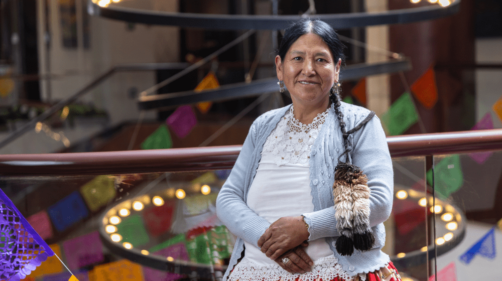 Una mujer con vestimenta tradicional y una larga trenza sonríe a cámara