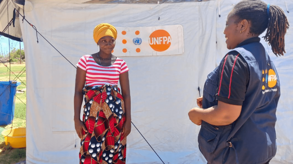  Una embarazada sonríe a una mujer que lleva un chaleco del UNFPA fuera de una tienda de campaña