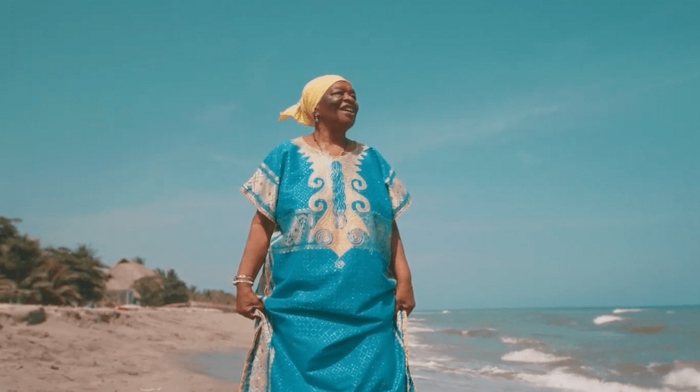 Una afrodescendiente con un vestido azul camina por la playa.