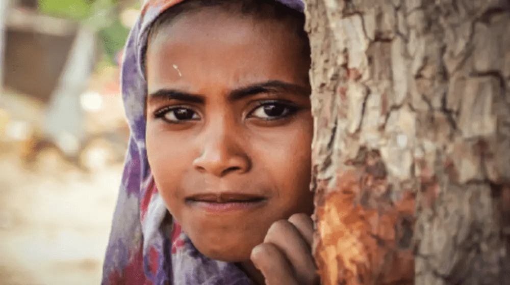 Young girl standing behind tree.