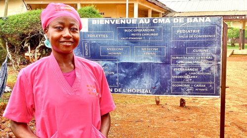 A midwife dressed in a pink uniform stands beside a sign.