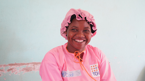 Une femme sourit, vêtue d’une blouse médicale rose