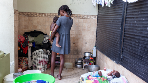 A displaced woman in a blue dress holds one of her children.