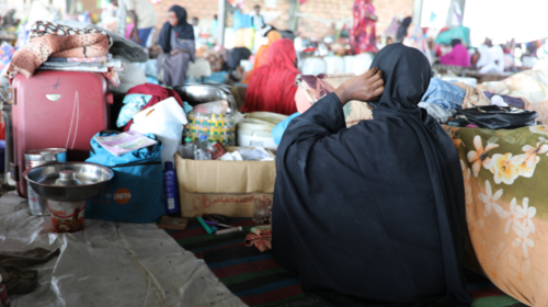 Varias mujeres sentadas con sus pertenencias en un refugio temporal al aire libre.